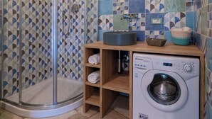 Un baño con cabina de ducha de vidrio, un lavabo con espejo, una lavadora y repisas con toallas.