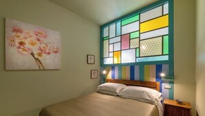 Un dormitorio con una cama, un ventanal de vidrio emplumado de colores y un cuadro en la pared.