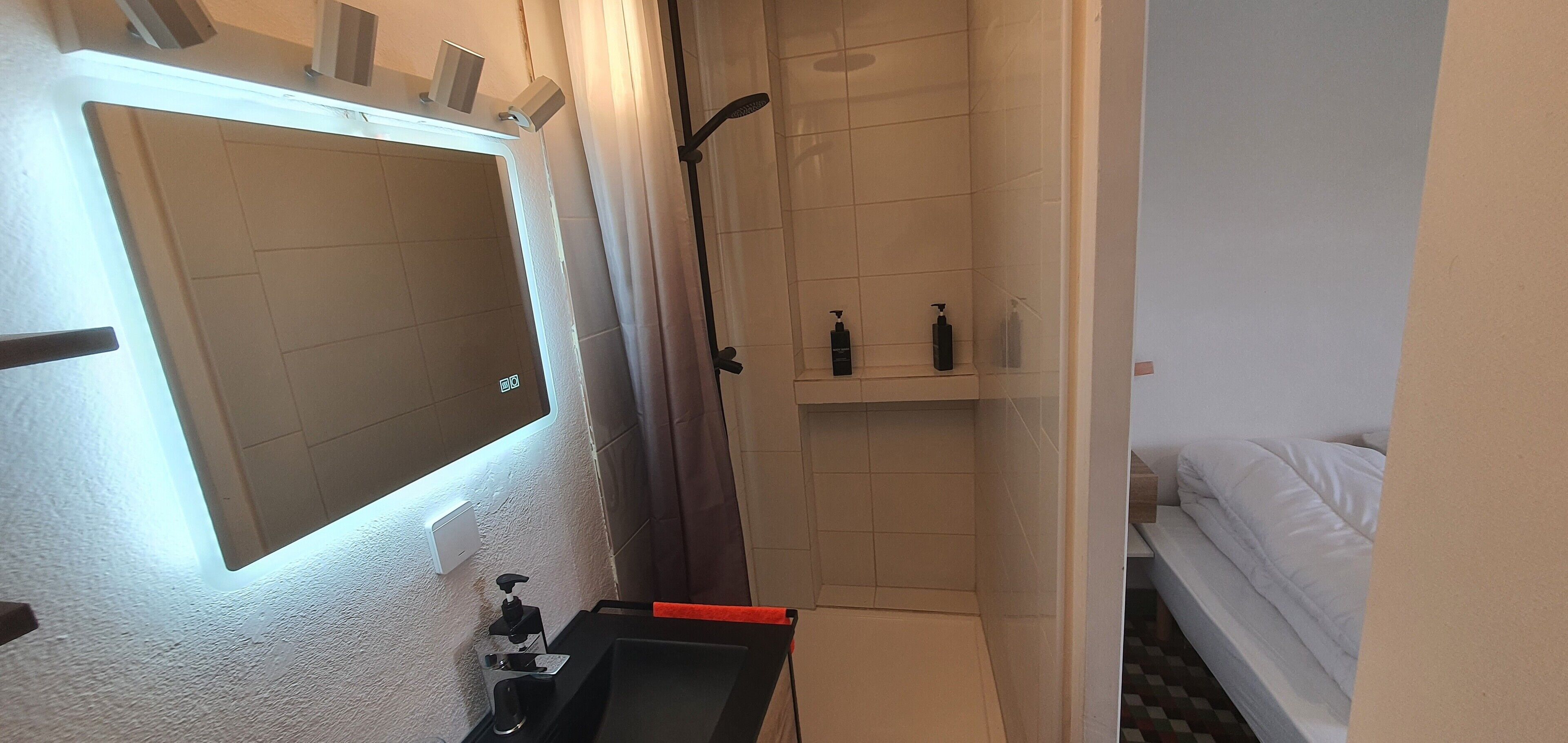 Ein kleines Badezimmer mit Spiegel, Dusche und Ablage für Pflegeprodukte.