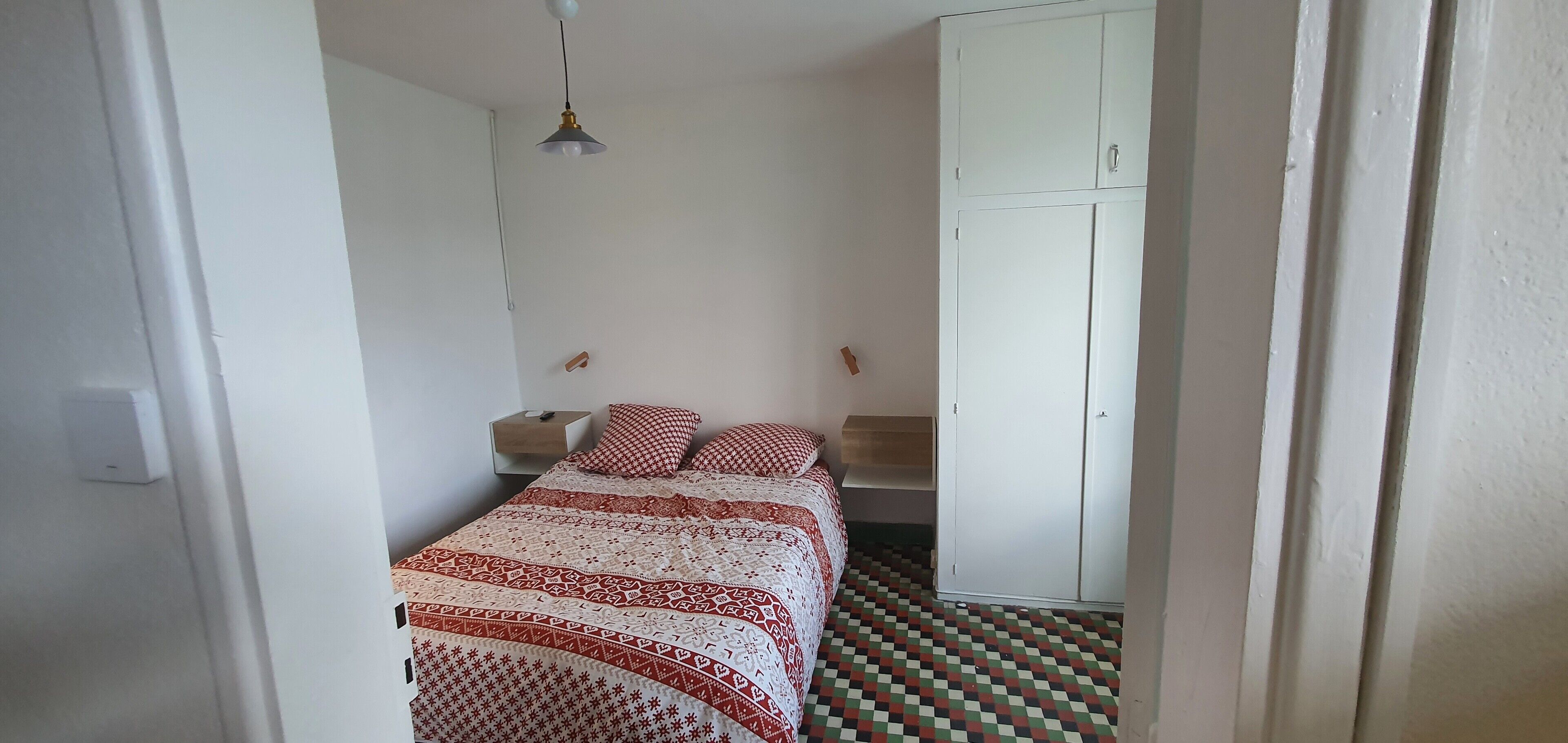 Une chambre à coucher comprenant un lit, une armoire, une table de chevet et un luminaire suspendu.