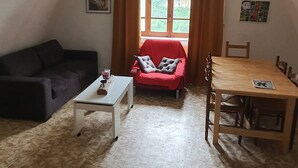 Una sala de estar acogedora con techo alto, un sofá, una mesa de centro, una mesa de comedor y una ventana con cortinas.