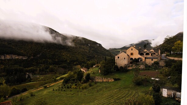 Un edificio de piedra con varios arcos, rodeado de campos verdes exuberantes y montañas.