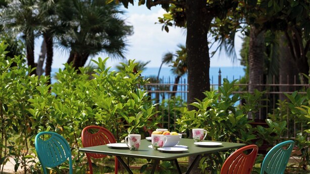 An outdoor dining area with a table set for four, surrounded by lush greenery and palm trees.