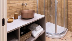 A bathroom with a curved glass shower enclosure, a round copper sink, and a built-in shelf with towels.