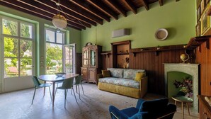 A spacious room with a large window, a wooden ceiling, a fireplace, and a dining area with a table and chairs.