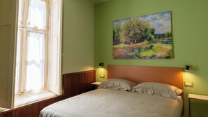 A bedroom with a bed, a window, and a painting on the wall.