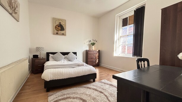 Een slaapkamer met een bed, nachtkastjes, een kaptafel, een bureau en een raam met gordijnen.