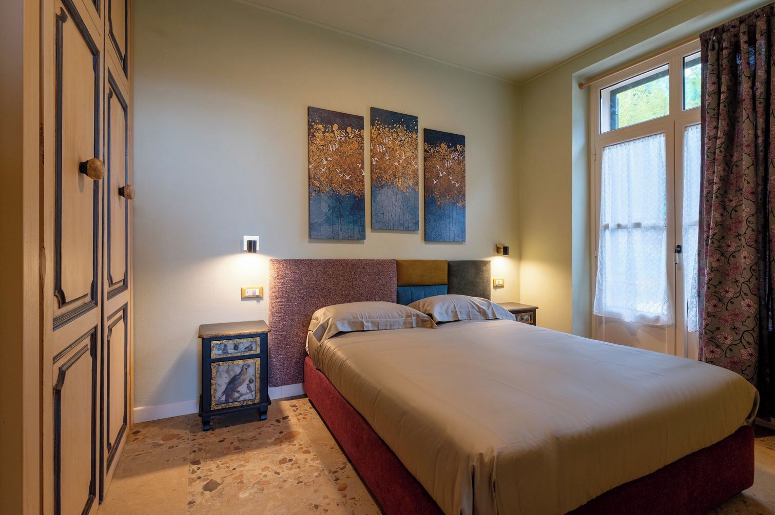 A bedroom with a bed, two bedside tables, a headboard, and three wall-mounted paintings.