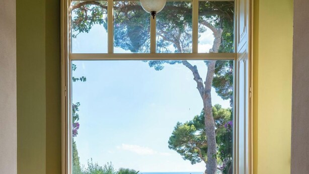 A room with wicker chairs, a small table, and a large window offering a view of the sea and buildings. - Apartment no. 3 ( CIN: IT008031B423CF7JSW Citra 008031-LT-1489 ) (Imperia)