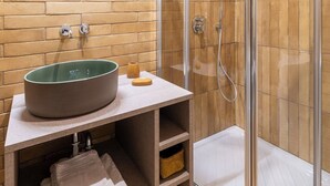 Ein Badezimmer mit einer Duschkabine aus gebogenem Glas, einem Waschbecken mit grüner Schale und einer gefliesten Wand.