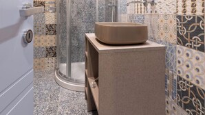Een badkamer met een glazen douchecabine, een ronde spiegel en een beige wastafel op een zuil.