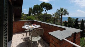 A balcony with a table and chairs, overlooking a coastal landscape with trees and the sea. - APARTMENT No. 9 ( CIN: IT008031B4324MG4G6 Citra 008031-LT-1495 ) (Imperia)
