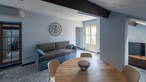 A modern living room with a gray sofa, a round wooden table, and a television in a separate room. - APARTMENT No. 9 ( CIN: IT008031B4324MG4G6 Citra 008031-LT-1495 ) (Imperia)