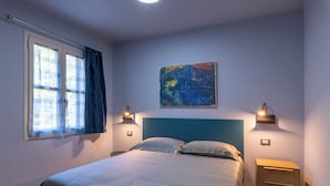 Un dormitorio con cama, dos mesitas de noche, una ventana con cortinas y un cuadro colgado en la pared.