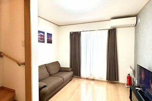 Una sala de estar con un sofá, un televisor de pantalla plana y un ventanal con cortinas.