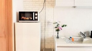 A kitchen with a microwave on a white cabinet, a sink with a vase of flowers, and a brick wall. - Kayo, Nijo Minami, 6 minutes walk from Nijo Station, quiet house (Kyoto)
