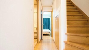 A narrow hallway with a wooden staircase on the right, leading to a room with a bed and a blue curtain. - Kayo, Nijo Minami, 6 minutes walk from Nijo Station, quiet house (Kyoto)