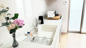 A modern kitchen with a white sink, a vase with flowers, and a microwave on a wooden shelf. - Kayo, Nijo Minami, 6 minutes walk from Nijo Station, quiet house (Kyoto)