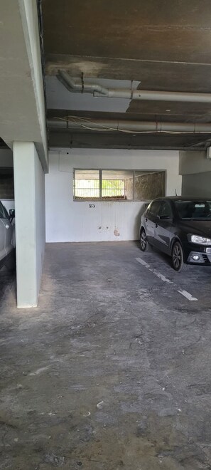 Een parkeergarage met betonnen vloer en muren, een raam met tralies, en een geparkeerde auto.
