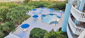Une piscine sur le toit, agrémentée de chaises longues et de parasols, entourée de verdure et d’une rambarde blanche.