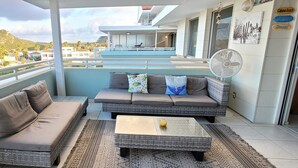 A balcony with wicker furniture, a fan, and a view of a building and palm trees. - Vistá Piscaderá (Willemstad)