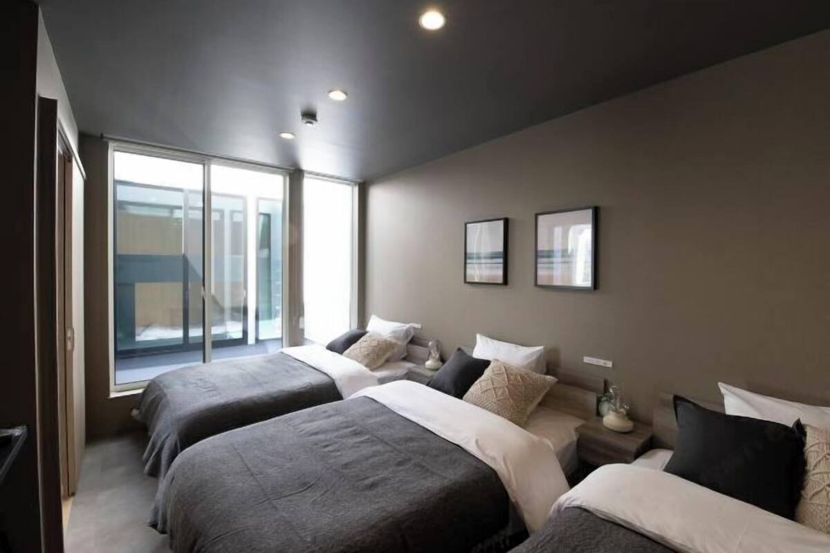 A modern hotel room with two beds, a large window, and a view of the city.