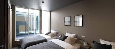 Quarto de hotel moderno com duas camas, uma janela grande e vista para a cidade.