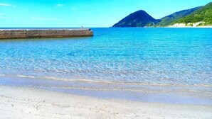 Una playa con aguas cristalinas, un muelle de madera y una montaña al fondo.