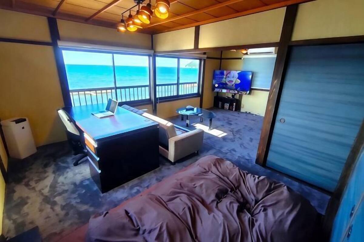 A room with a bed, a desk, a chair, a TV, and a view of the ocean.