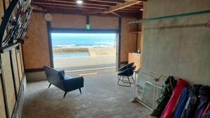 Una habitación con vista a la playa, una silla negra, una mesa y un perchero para maletas.