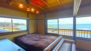 Una habitación con cama, una mesita pequeña y ventanas amplias con vista al océano.