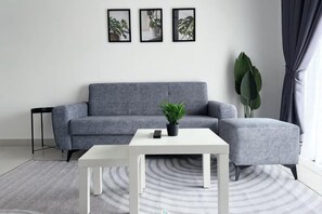 Een moderne woonkamer met een grijze bank, een witte salontafel en een potplant.