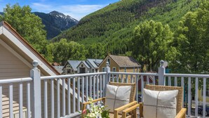 A balcony with wicker furniture and a vase of flowers, overlooking a forested mountain area.