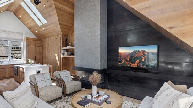 A modern living room with a fireplace, wooden ceiling, and a large TV mounted on the wall.