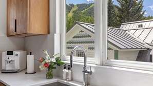 A kitchen with a built-in sink, a coffee maker, and a window with a view of a house and hills.