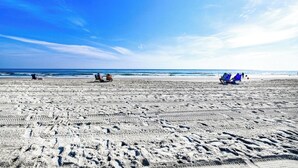 A wide sandy beach with footprints, a clear blue sky, and a calm sea. - Reunion Villas #3 - Four Bedroom Three Bath, Second Row with Community Pool (Garden City Beach)