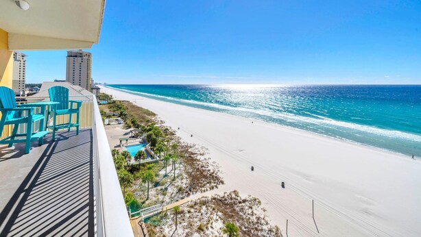 A balcony with turquoise chairs overlooking a beach with a clear view of the ocean and distant buildings.
