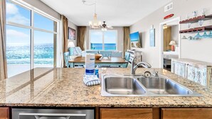 A kitchen with granite countertops, stainless steel sinks, and a dining area with a view of the ocean.