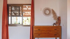 Ein Zimmer mit einem hölzernen Schminktisch, einem Fenster mit Vorhängen und einem Wandbild.