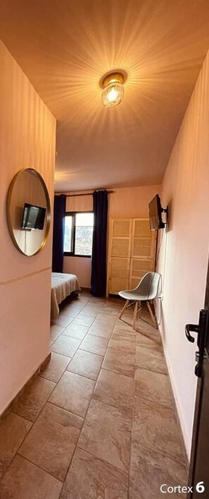 Un pasillo estrecho con una cama, una silla, un televisor y un armario.