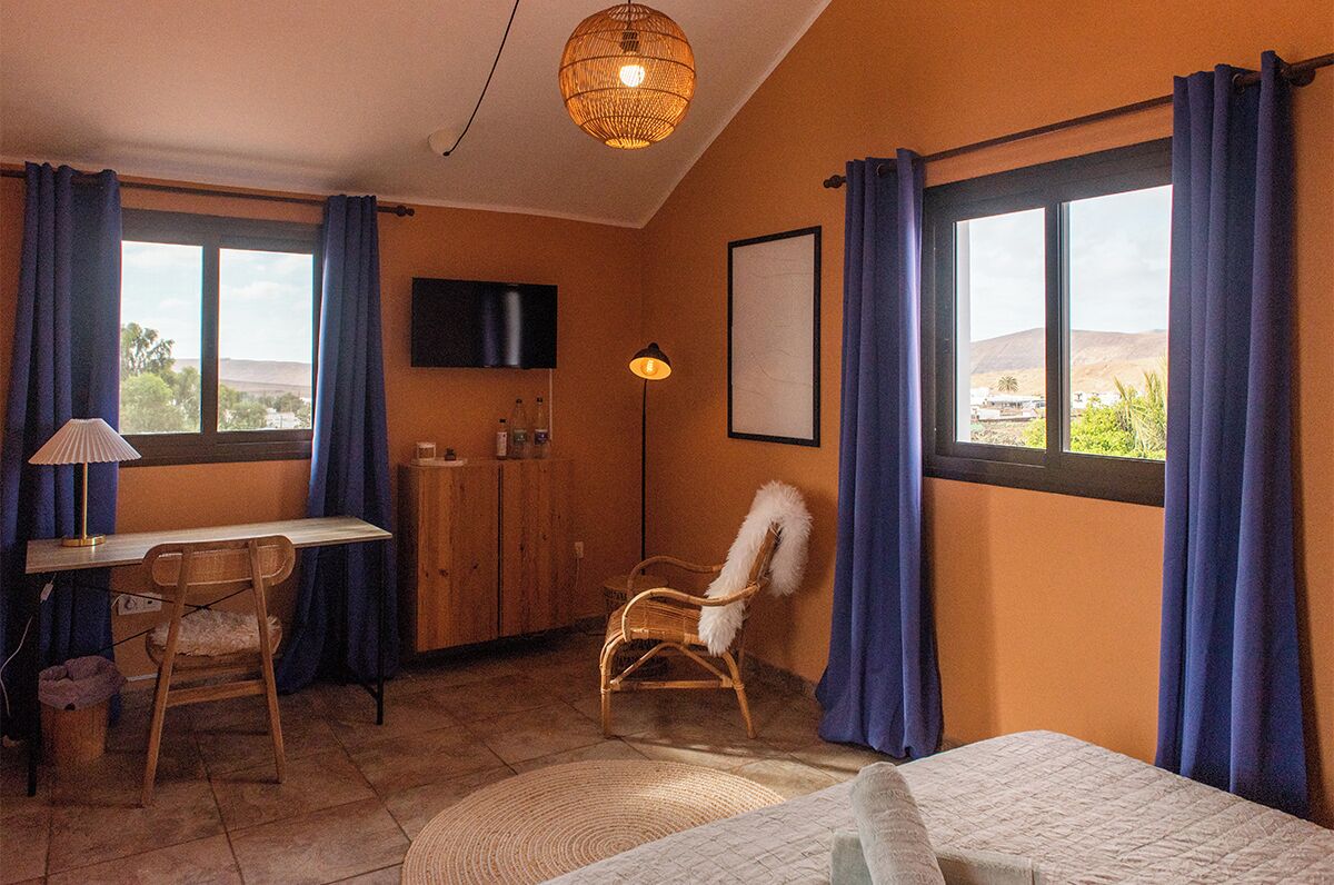 A room with a bed, a desk, a chair, a television, and a window with curtains.