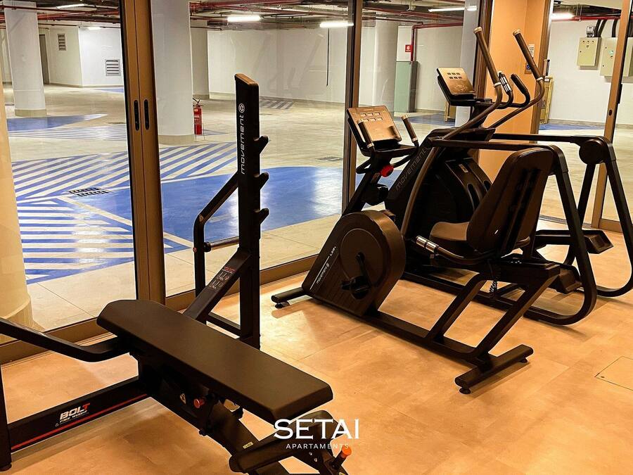 Un gimnasio con equipamiento de ejercicio, una banca y una máquina fijada a la pared.