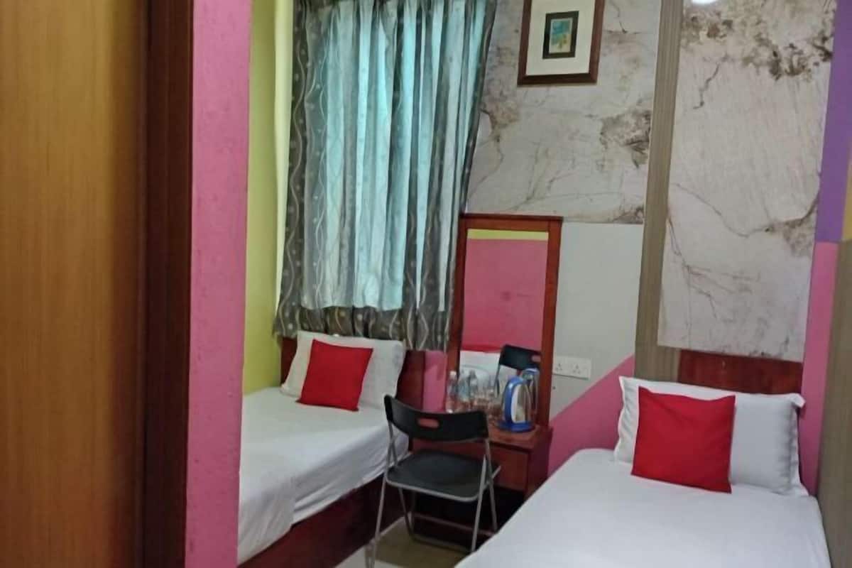 Ein Hotelzimmer mit zwei Betten, einem Sessel, einem Schreibtisch mit Spiegel und einem Fenster mit Vorhängen.