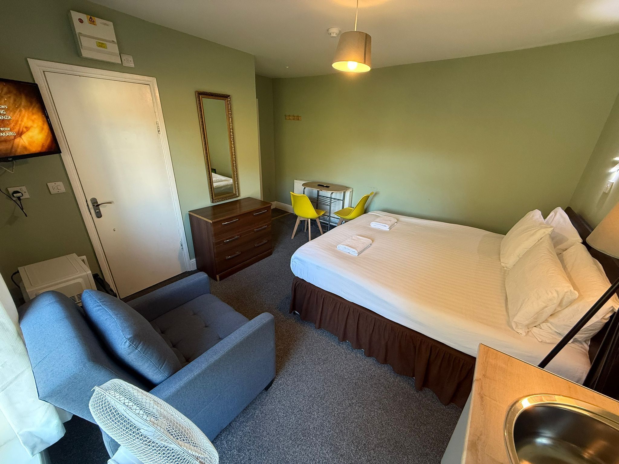 A hotel room with a bed, a dresser, a desk with a chair, a sofa, and a mirror.
