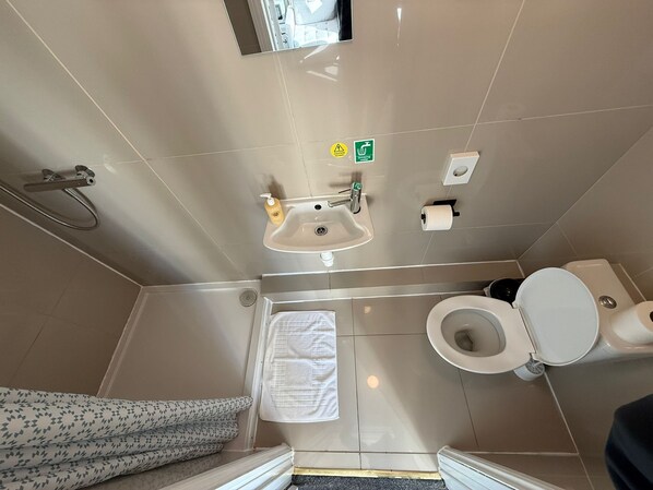 Une salle de bain comprenant des toilettes, un lavabo et une douche. On y trouve également un porte-serviettes et un support à papier toilette.