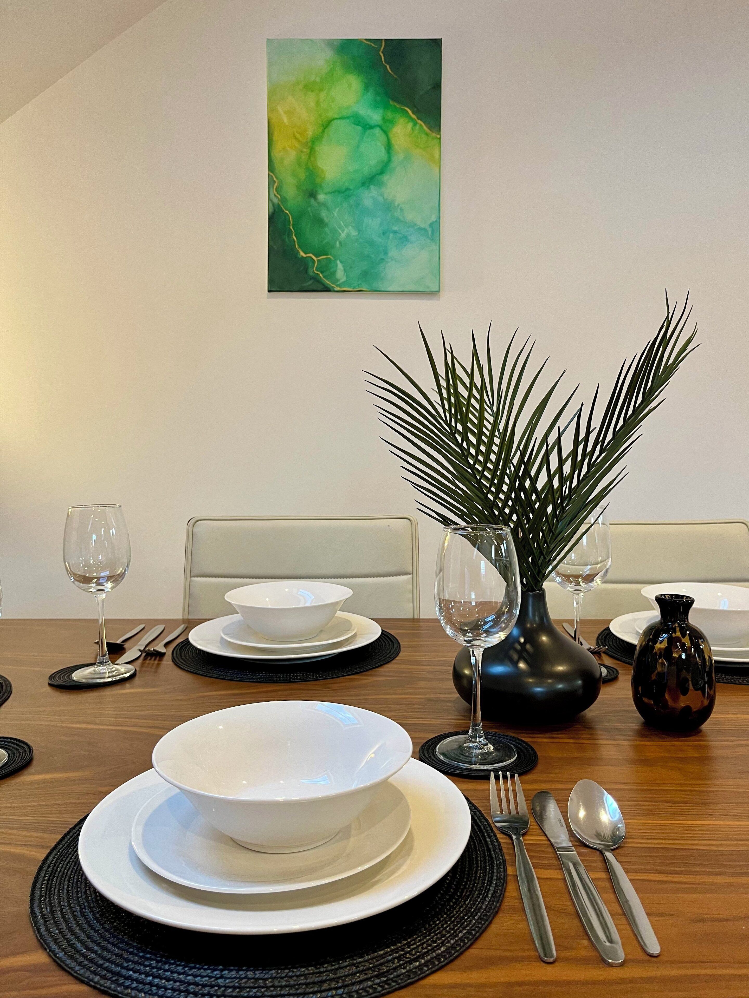 Et spisebord dækket med tallerkener, skåle, bestik og en vase med en plante.