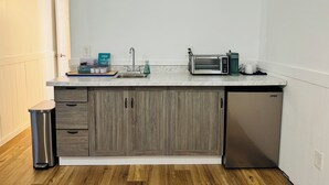 Una cocina equipada con lavavajillas, microondas y tostadora. Hay un cubo de basura y una pequeña encimera con dispensador de jabón.