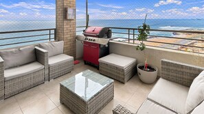 A balcony with wicker furniture, a barbecue grill, and a view of the sea.
