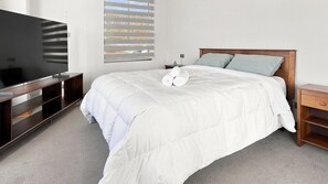 A hotel room with a bed, a TV, and a window with blinds.