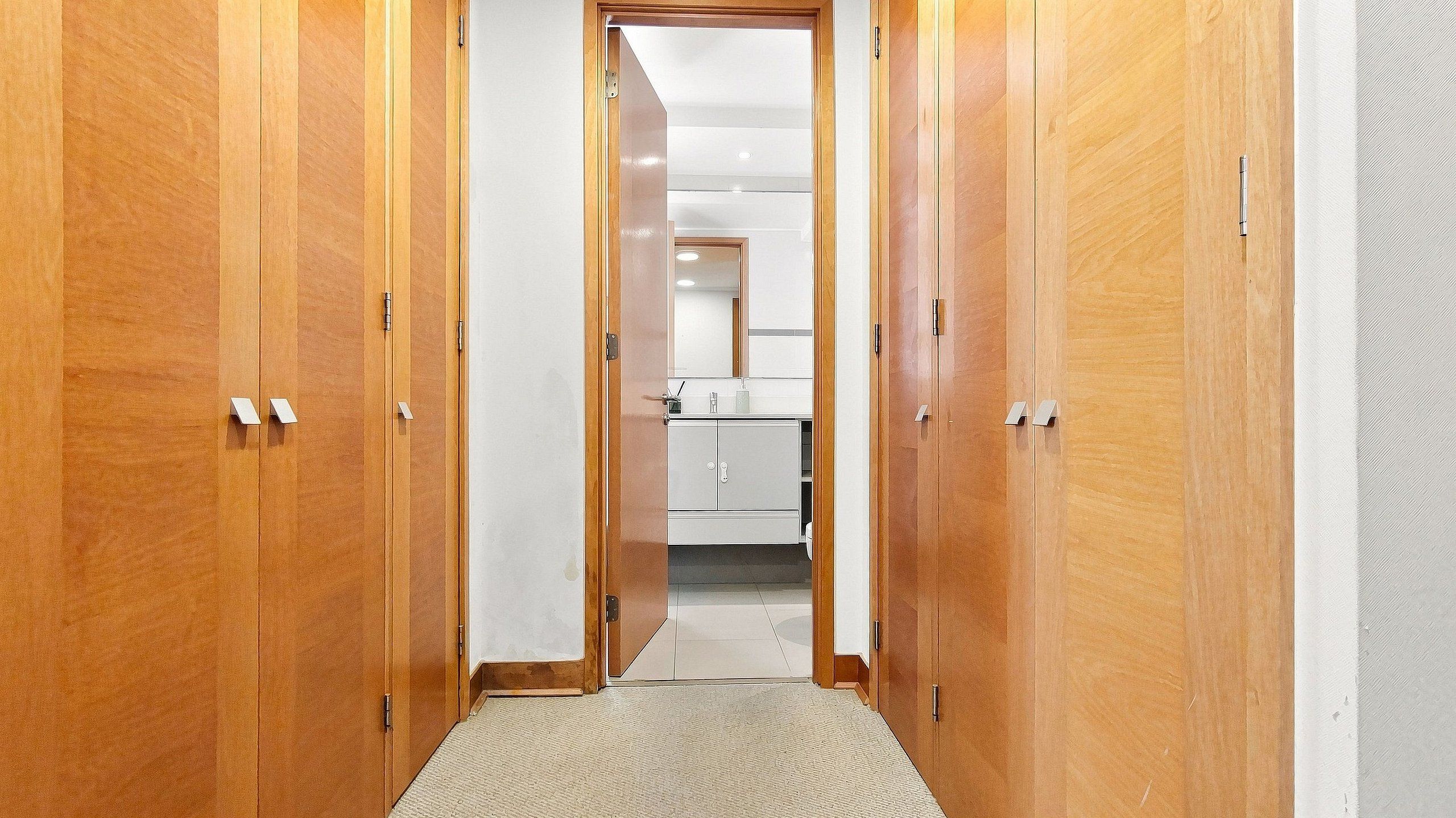 A hallway with wooden doors leading to a kitchen area.
